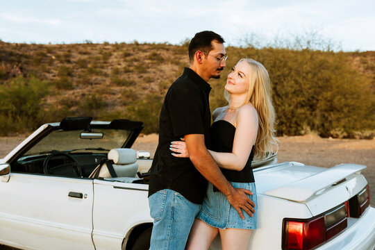 Young couple hugging in desert in front of convertible