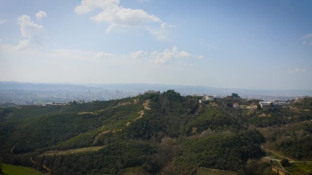 Cinematic aerial drone reveal of Tirana, Albania, filmed from Dajti National Park as lush green hills open up to a distant urban skyline. 