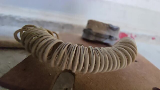 Macro shot of a vintage heating element coil with ceramic insulator and wires on a wooden base.