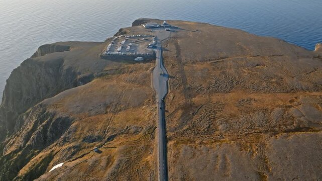 Drone aerial approaching the Nordkapp visitor centre and parking area in northern Norway. Remote Arctic landscape spreads across the windswept plateau.
