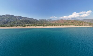 Obraz premium Aerial view of a stunning Mediterranean coastline featuring crystal clear turquoise waters - pristine sandy beach - and dramatic mountainous landscape under blue sky