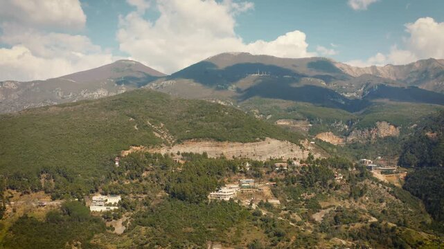 Smooth forward drone footage ascending toward Dajti Mountain in Albania, showcasing lush green scenery, winding casual roads, and distant clouds on a sunny day.