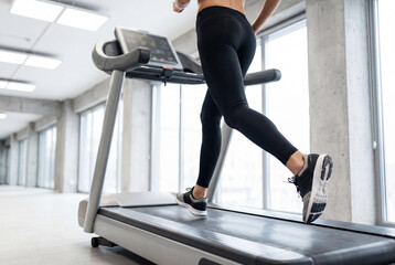 Fototapeta premium Close up of a fit woman running on a treadmill in a modern gym for cardio workout