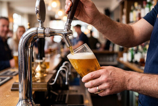 Bartender pouring golden beer into pint glass from tap
