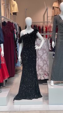Storefront window with two mannequins wearing grey wrap and pink textured shift mannequins on pedestals with clothing racks in background contrasting