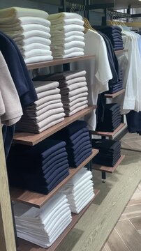 Folded shirts on wooden shelves neatly stacked in navy white beige tones, layered board display with smooth fabric edges and tidy presentation