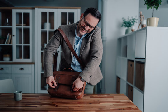 Busy man talking on phone and organizing briefcase, getting ready for work from home or leaving office