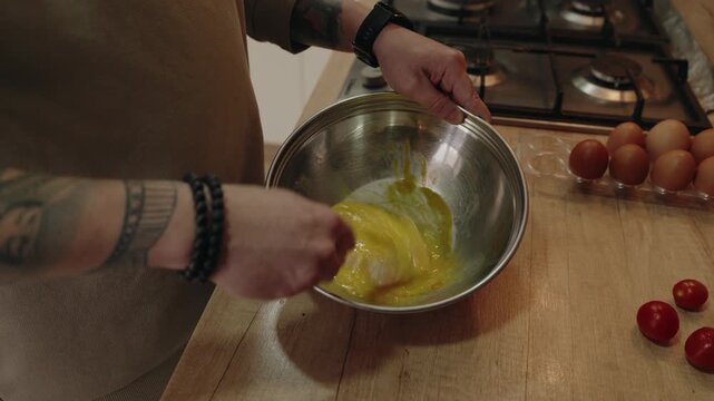 A Person Whisking Fresh Eggs in a Metal Bowl on a Wooden Kitchen Counter