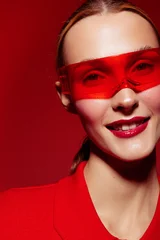 Close-up of smiling woman wearing red sunglasses and red outfit on red background. Fashion portrait with vibrant colors and confident expression. Concept of style and modern look. © SHOTPRIME STUDIO