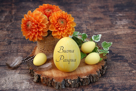 Buona Pasqua &ndash; Auguri di Pasqua italiani con dalie e uova gialle su un disco di legno rustico.