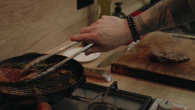 Hand Flipping a Perfectly Cooked Steak with Tongs on a Hot Pan in a Kitchen