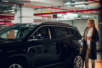 Businesswoman unlocking car in underground parking garage, holding coffee cup during daily commute...