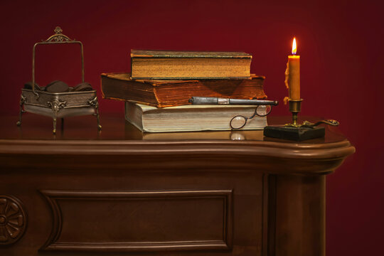 Antique still life with vintage books, candle, eyeglasses and cookies in decorative bowl on wooden cabinet.
