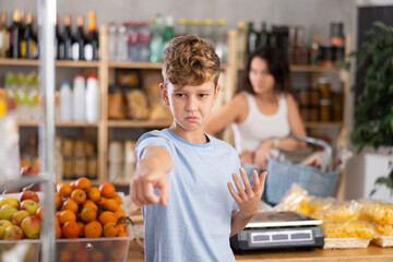 Sad and angry boy stands near window of candy store. Disgruntled mother screams and scolds boy, reproaches him. Mom scolds boy, does not allow him to buy sweets © JackF