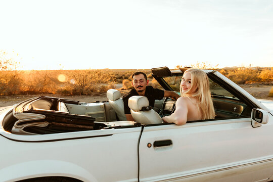 Couple sitting in convertible car looking back