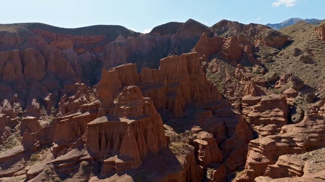 Wide aerial view of rugged rock formations in Kyrgyzstan's canyon. Layered eroded rocks and sparse vegetation create a majestic, desolate landscape.