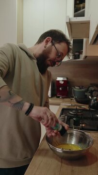 Bearded Man in Glasses Seasoning Eggs in a Bowl While Cooking in a Modern Kitchen