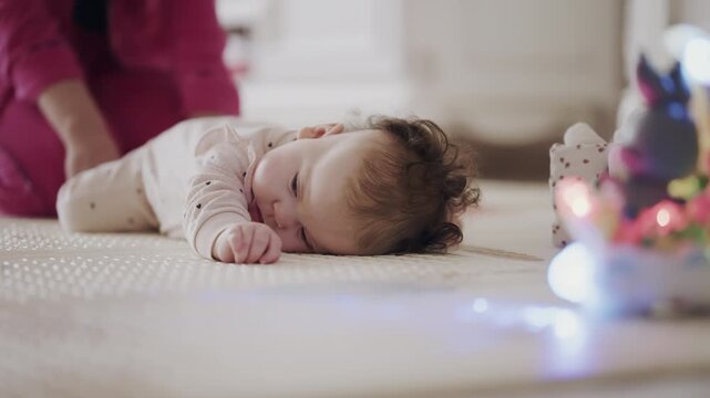 Close up of infant lying on play mat during playtime while caregiver assists nearby