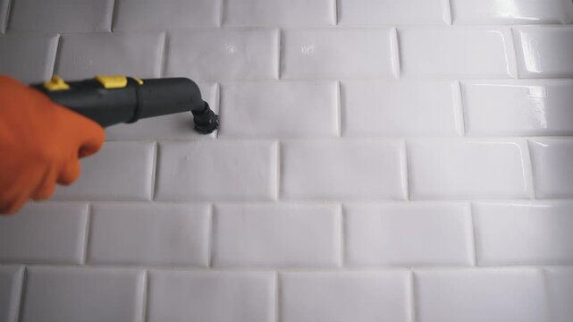 Close up of a person deep cleaning kitchen grout on white subway tiles. Using a steam cleaner for sanitation, this highlights hygiene, housework, and modern cleaning methods. Neutral color palette.