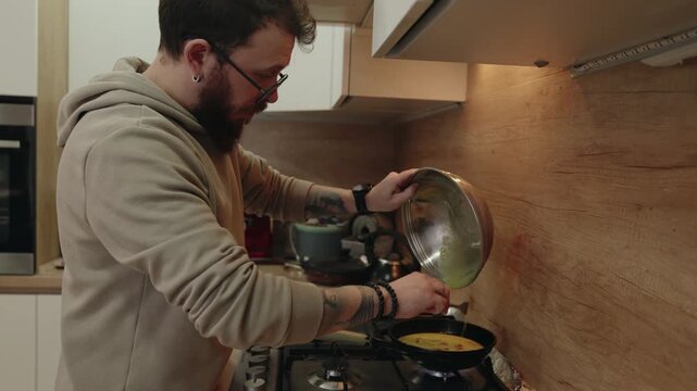 Man Preparing Breakfast, Pouring Whisked Eggs From Bowl Into Hot Frying Pan On A Gas Stove.