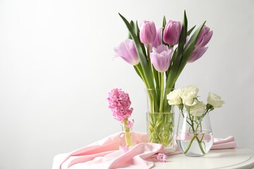 Fototapeta premium Beautiful flowers in vases on white table against light background. Space for text