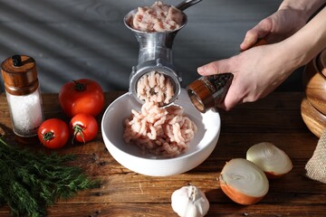 Woman adding spices into bowl with chicken mince and manual meat grinder at wooden table, closeup