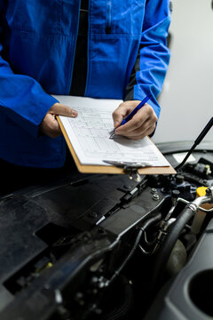 Mechanic writing vehicle service report over open engine compartment