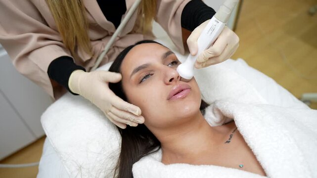Professional cosmetologist performing a non invasive radiofrequency lifting procedure on a young woman's face, stimulating collagen production for a rejuvenating and anti aging effect