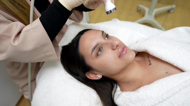 Beautiful woman receiving a rejuvenating radiofrequency facial treatment from a cosmetologist in a modern beauty clinic for skin tightening, lifting, and anti aging effects