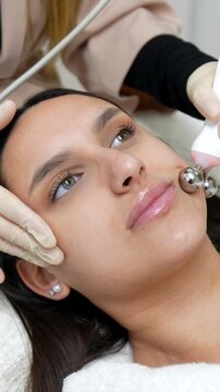 Professional cosmetologist performing a stimulating microcurrent facial massage on a young woman's skin to promote circulation, reduce puffiness, and provide a lifting effect for rejuvenation