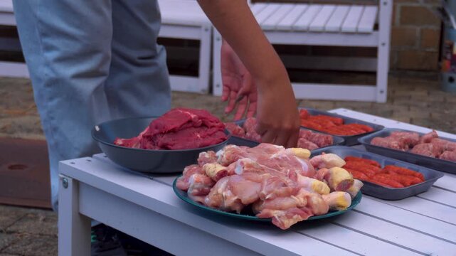 On the table are plates of meat, such as cold cuts and chicken, as well as chopped vegetables for preparing the meal: barbecue