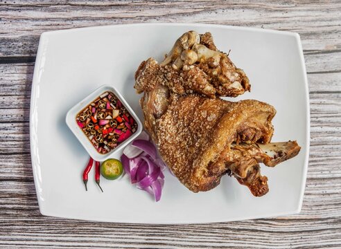 A crispy deep fried pork leg served with dipping sauce and fresh side ingredients