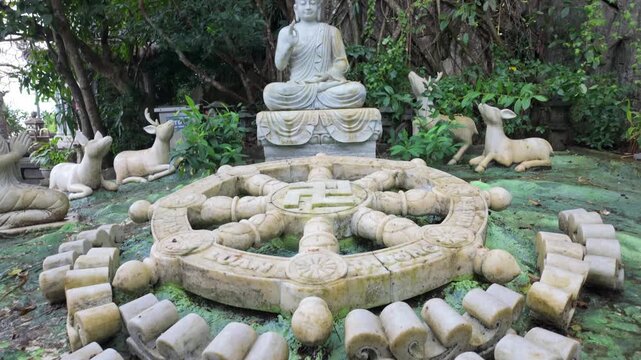 A serene Buddha statue sits in meditation pose, surrounded by deer sculptures and a Dharma wheel, symbolizing Buddhist teachings in Marble Mountain, Da Nang, Vietnam.