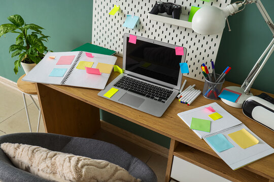 Workplace with blank laptop, sticky notes and pegboard near green wall in office