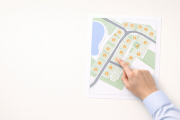 Obraz premium Person pointing at residential area map with house and roads, planning neighborhood layout with green spaces and water body, concept of real estate or urban planning