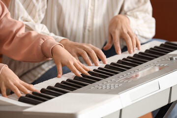 Fototapeta premium Female music teacher giving synthesizer lesson to little girl at home, closeup