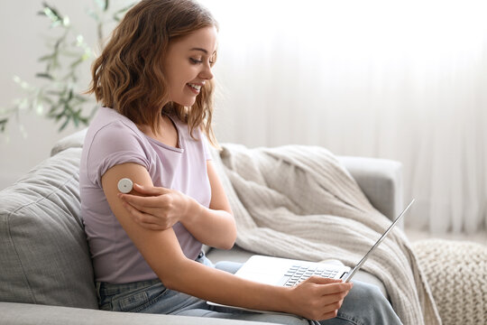Diabetic young woman with glucose sensor talking to doctor online on sofa at home