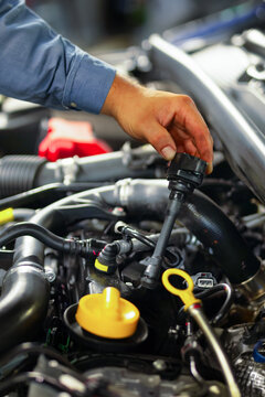 Mechanic removing ignition coil from petrol engine in professional auto repair workshop close-up