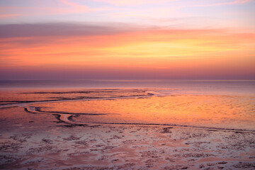 Obraz premium Mudflat reflecting warm colors of a sunset sky, showing textured patterns of the exposed seabed at low tide