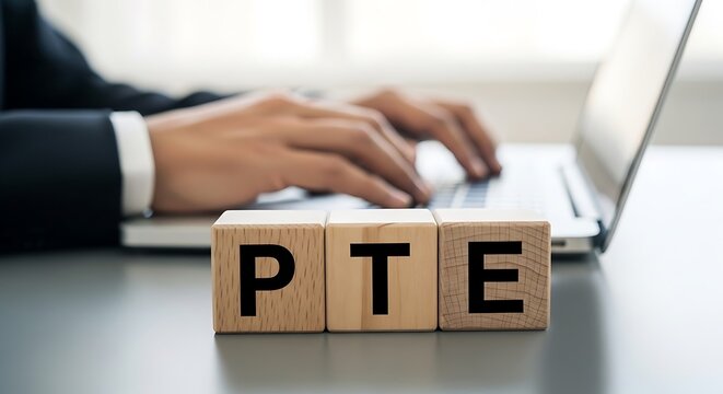 Businessman typing on laptop with 'pte' wooden blocks, symbolizing english language test for professionals