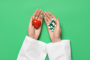 Fototapeta premium Female doctor's hands with red heart and different pills on green background