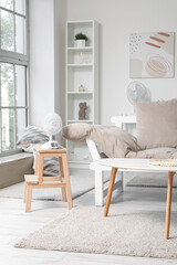 Interior of light living room with couch and electric fan on stepladder