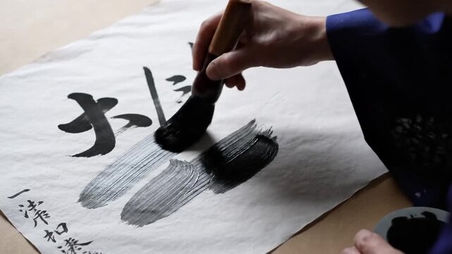 Close-up of an artist painting Japanese calligraphy with a brush on white paper.