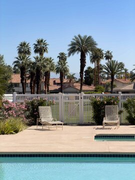 Empty lounge chairs invite you to spend time by the pool in a beautifully manicured palm desert neighborhood full of palm trees.