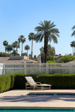 Empty lounge chair invites you to spend time by the pool in a beautifully manicured palm desert neighborhood full of palm trees.