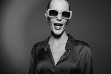 Obraz premium Stylish white woman with pale skin wearing large sunglasses and dark blouse poses confidently in monochrome studio portrait.