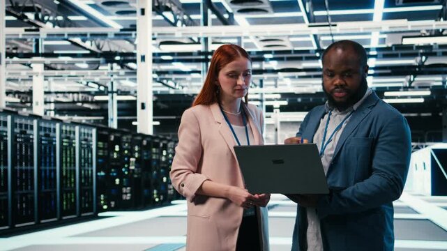 Server farm manager teaching intern to use laptop and optimize electronics during induction. Data center team leader and trainee using notebook to monitor system performance, camera A