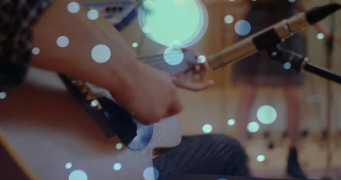 Seated guitarist strumming into mic, recording and alternating chords with bokeh over hands
