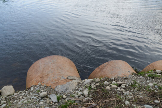 Rusty concrete pipes discharge water into a calm river, surrounded by rocks and sparse vegetation. Concept for environmental impact, water flow, and nature interaction.