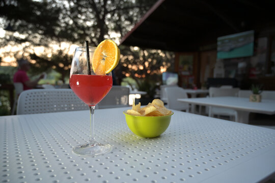 cocktail alcolico rosso in un bicchiere con una fetta d'arancia servito in una pineta vicino al mare in una sera d'estate